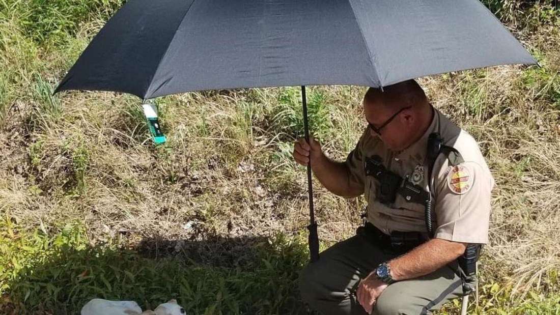 Ein Polizist hält einen Schirm über die Hündin, neben der er sitzt.