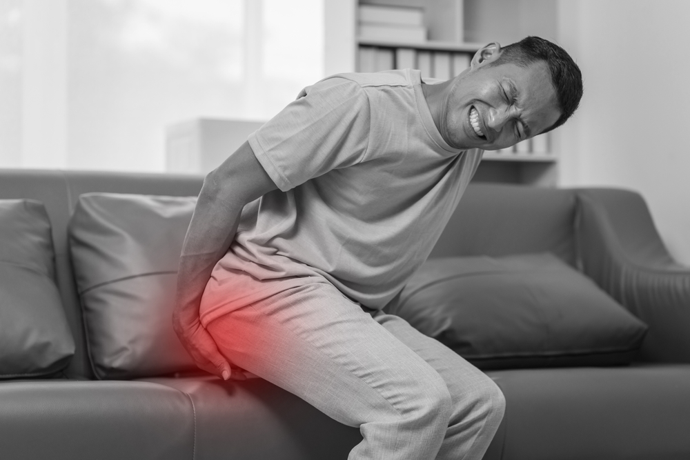 Middle-aged Asian Indian man with butt pain, hemorrhoids, colon pain, sitting on a sofa.
