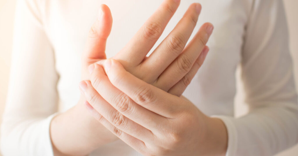 Young female in white t-shirt suffering from pain in hands and massaging her painful hands