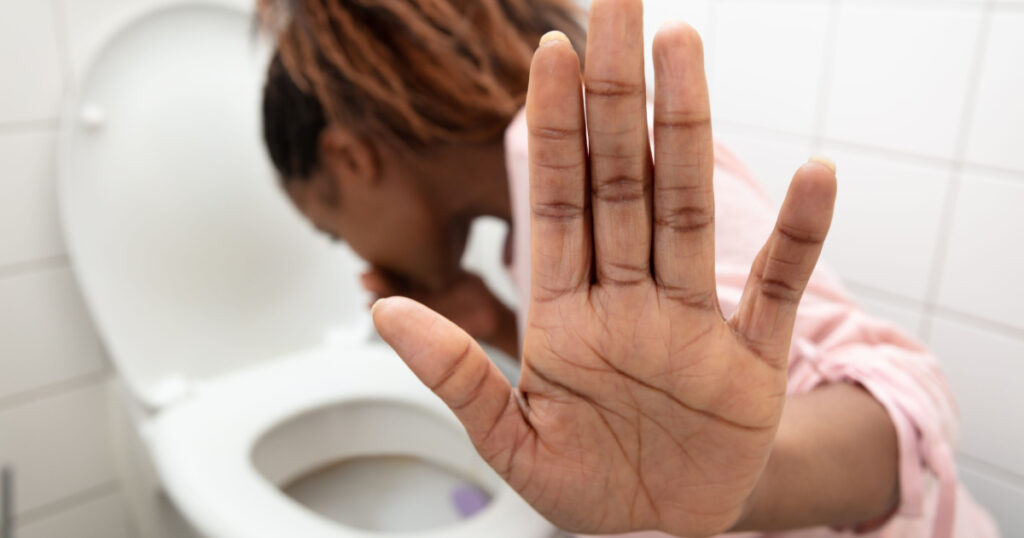 Close-up Of A Young Woman Showing Stop Sign While Vomiting In Toilet Bowl